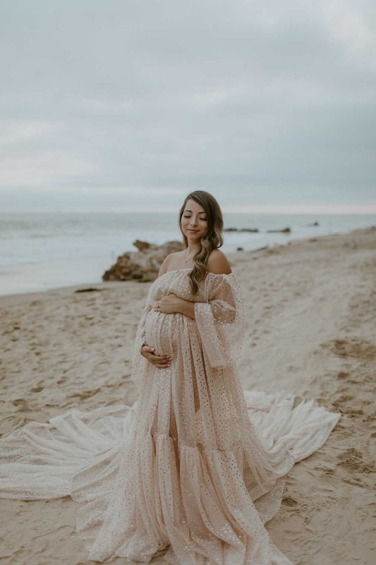 Lady posing holding her baby bump in long flowy tulle gown on the beach